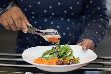 Eine Person schlichtet Salat vom Salat-Buffet auf ihren Teller: Feldsalat, Karottensalat, Pilze, Sprossen