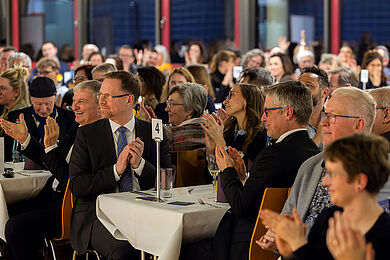 Blick in den Gastraum, Gäste lachen und klatschen.