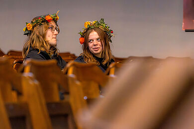 Personen mit Blumenkränzen auf dem Kopf unterhalten sich in der Philippuskirche