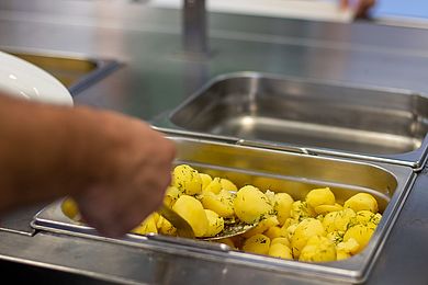 Ein Mitarbeitender serviert Kartoffeln auf einen Teller