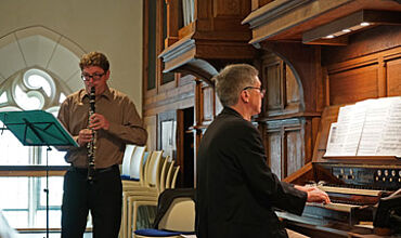 Zwei Personen musizieren - ein Mann spielt Klarinette und der zweite Mann spielt daneben an einer Orgel