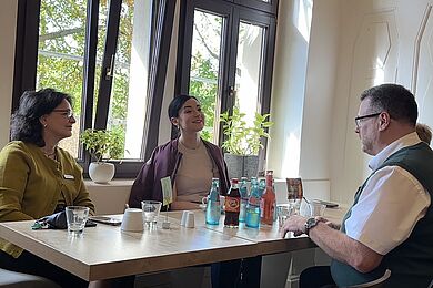 Im Gespräch im Frühstücksraum: Alicia Mellado, Dr. Paula Piechotta und Enrico Haußmann. Auf dem Tisch stehen verschiedene Getränke
