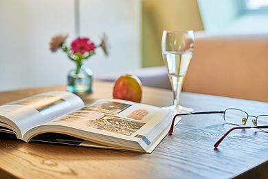 Detailaufnahme aus der Suite: Buch, ein Glas Sekt, Blumen, eine Brille und ein Apfel auf einem Tisch