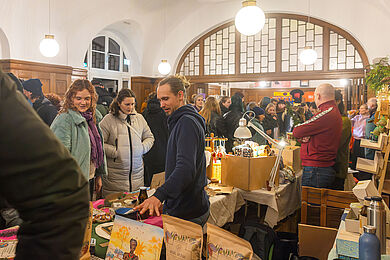 Blick in den Historischen Saal mit vielen Besucher*innen und Verkaufsständen