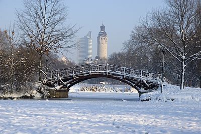 Leipziger Johannapark im Schnee. Man sieht eine Brücke, dahinter das neue Rathaus und den MDR-Turm